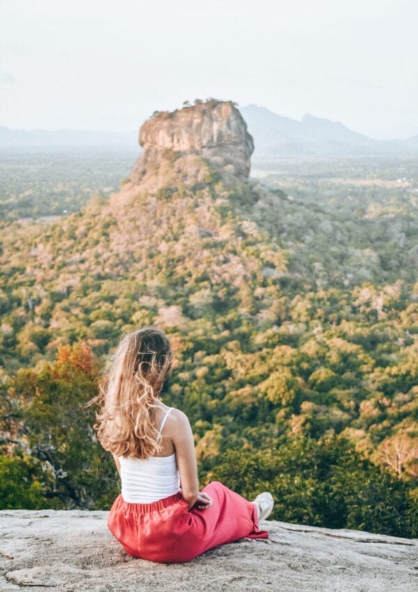 Girl sitting on rock looking out to Lion Rock, Sri Lanka.